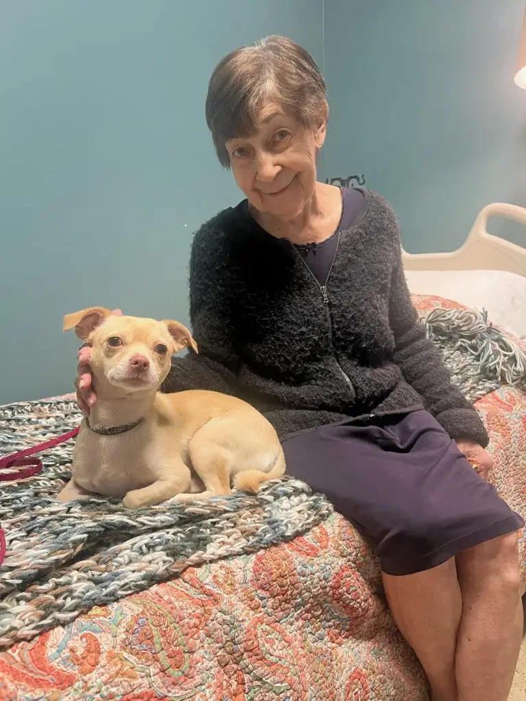 Adelaide smiling on her bed at the Shelter Home with a small dog